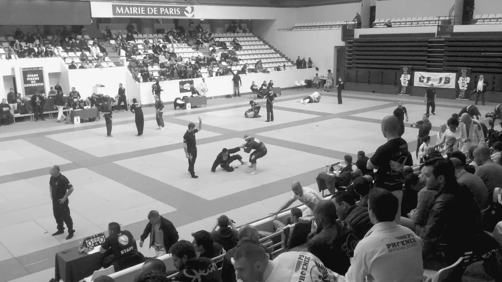 A wide view of a Brazilian Jiu Jitsu competition venue with several mats and rows of spectators.