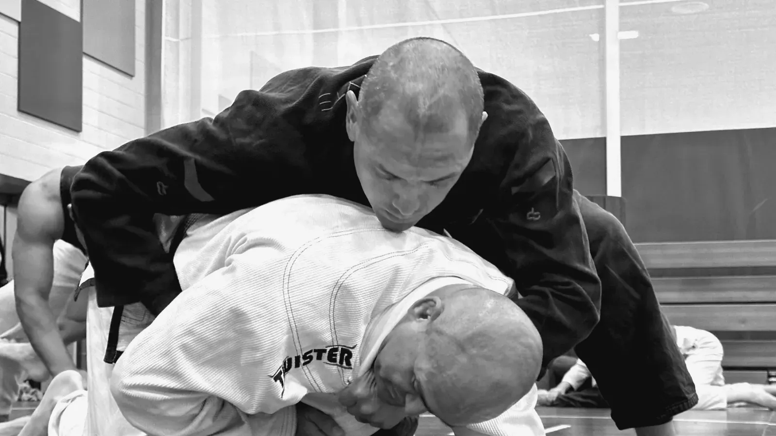 Two grapplers in gis, one holding a top control position on the ground.