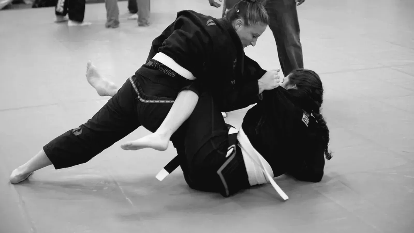 Brazilian Jiu Jitsu practitioners gi women rolling while training on the mat.