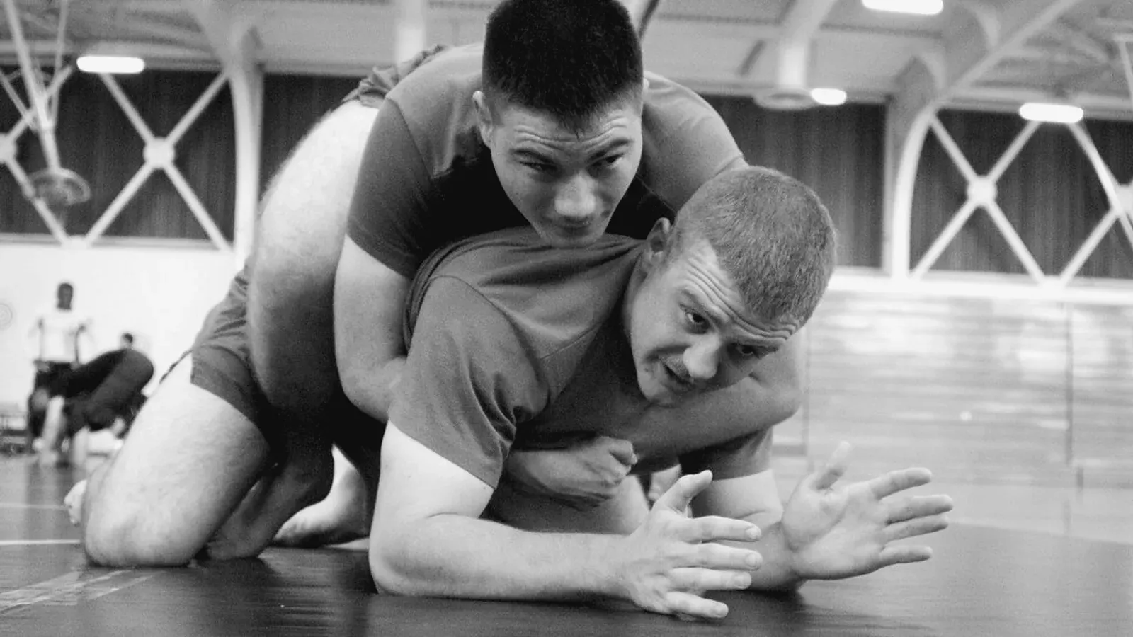 Grappling partners working together on the mat in a training hall.