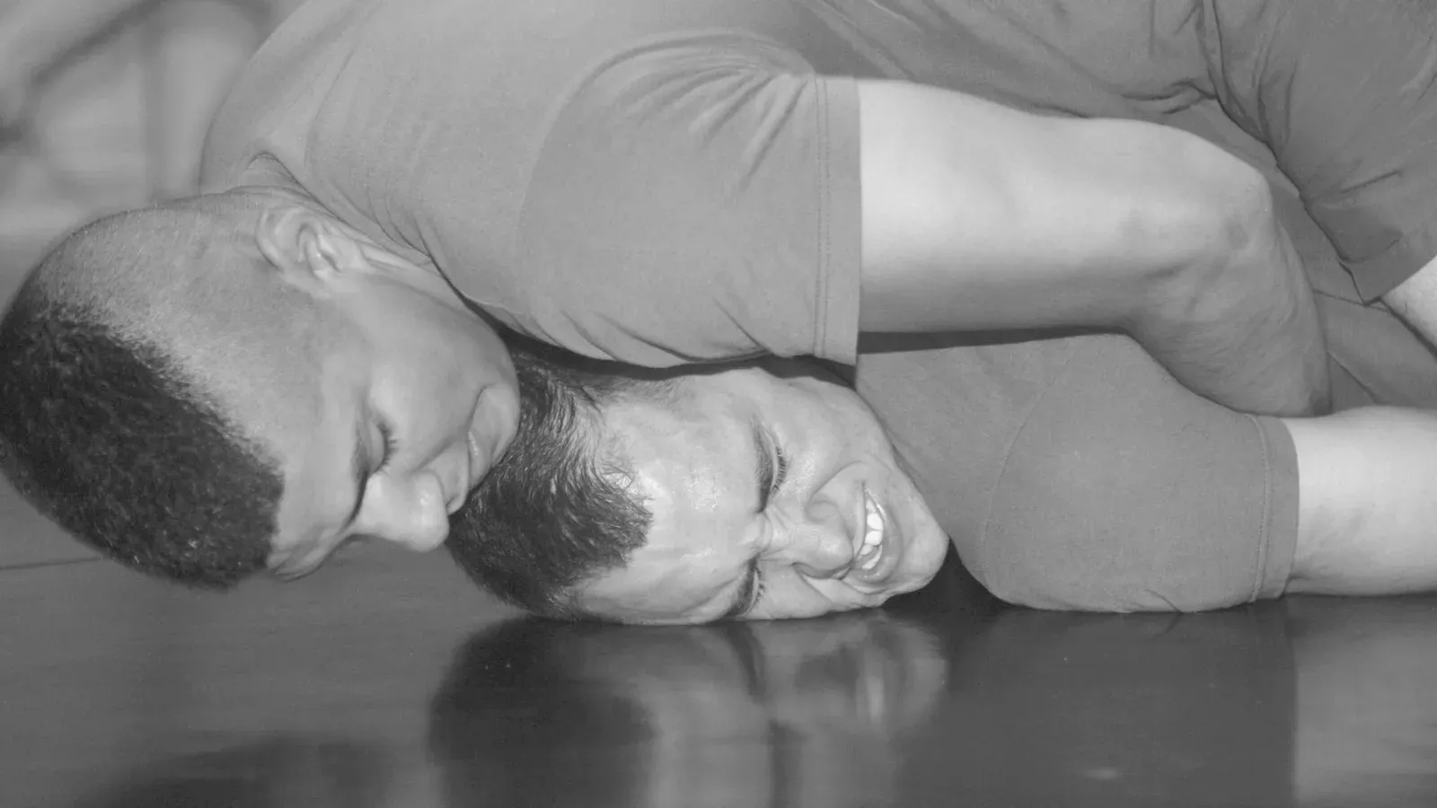 A close view of two grapplers on the ground, the top one pressing his weight down through his chest and shoulder.