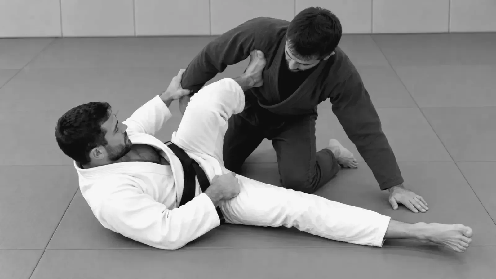 Gi partners practicing grips and leg positioning for a sweep from guard.